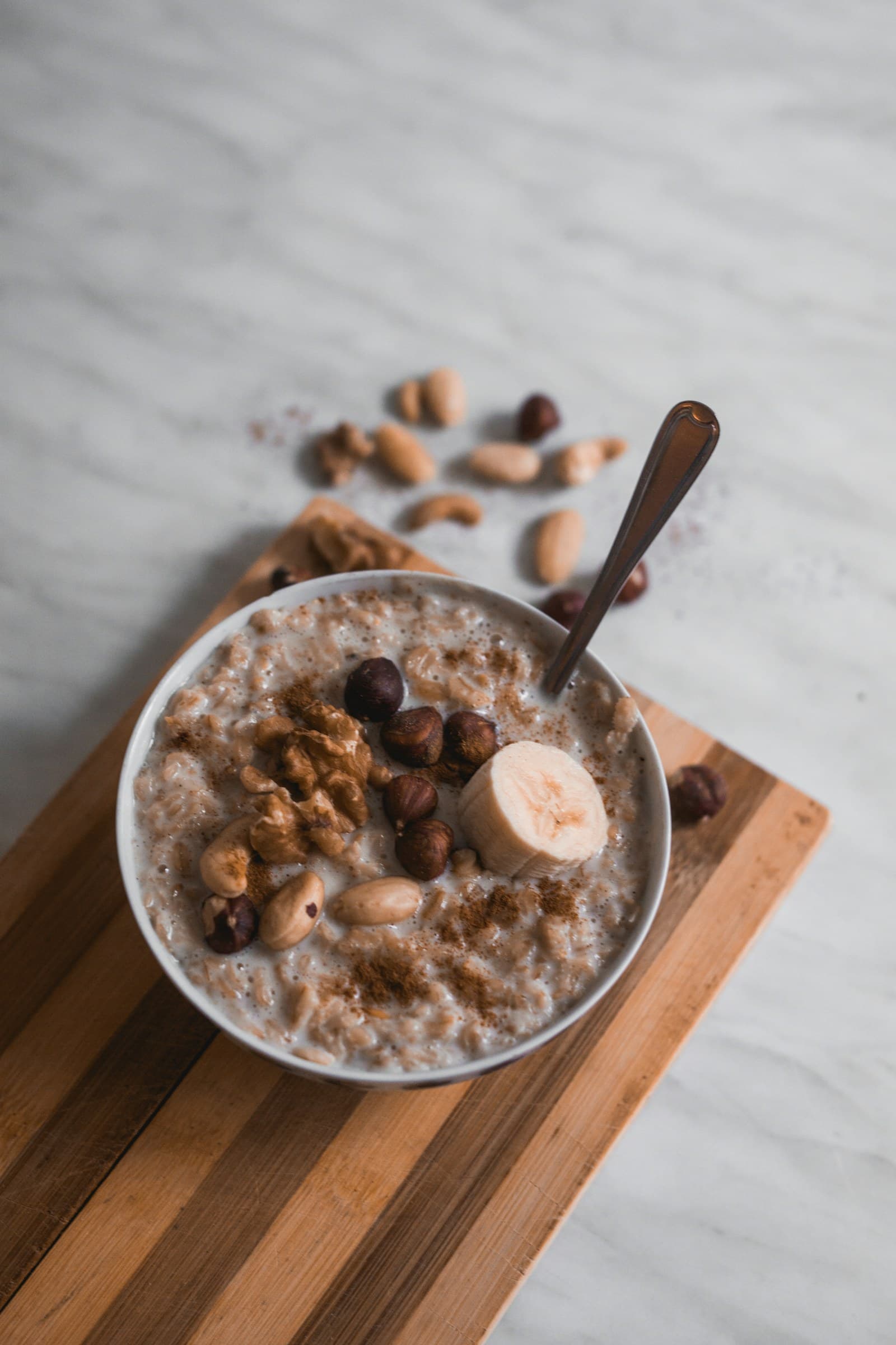 A bowl of oats topped with banana, walnuts and hazelnuts on a wooden board